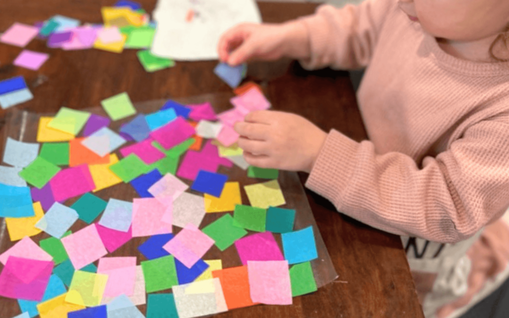 child placing colorful tissue squares on contact paper